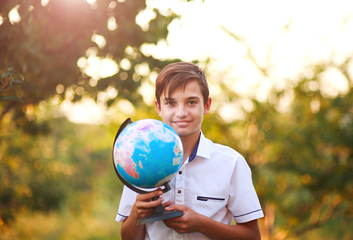 Smiling boy teenager holding a globe of planet earth in a summer park on a background of the nature trees at sunset, concept save the planet
