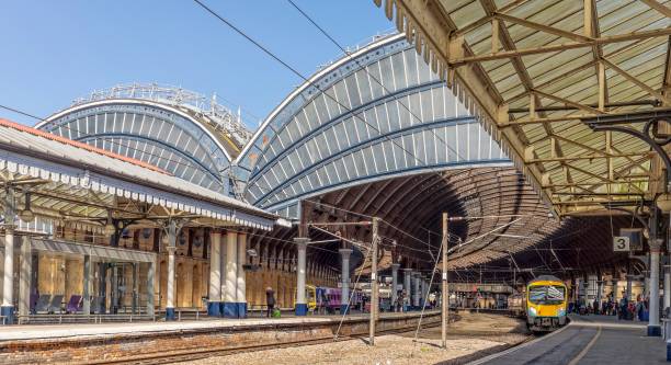Image of a 19th Century intricately designed railway canopy curving above the platform.  A train waits to depart. Classic view of a railway station.  A train is at the platform waiting to depart.  Overhead are ornate 19th Centrury canopies. york yorkshire stock pictures, royalty-free photos & images