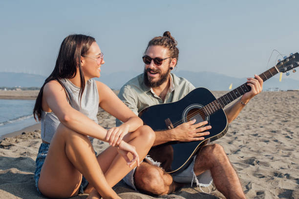 istock Young couple with a guitar sitting on a beach 1026040108