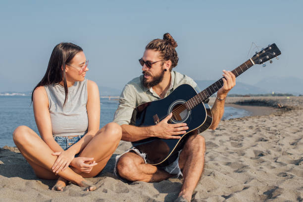 istock Beautiful young couple with a guitar sitting on a beach 1026040130