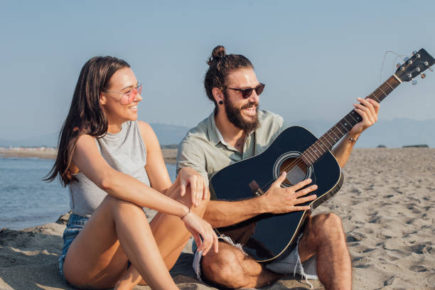 istock Smiling young couple with a guitar sitting on a beach 1026040178