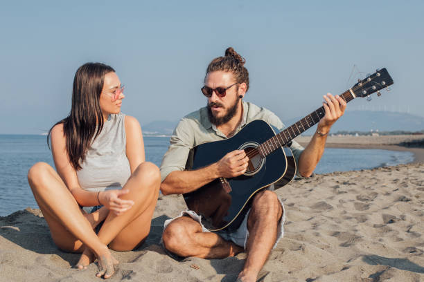 istock Romantic young couple with a guitar sitting on a beach 1026040184
