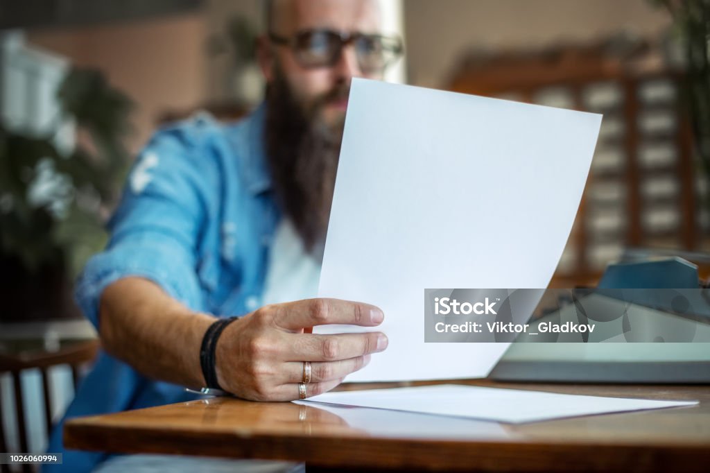 Bearded stylish writer reading his novel Bearded stylish writer reading his novel. Modern writer in glasses working on new book in library Letter - Document Stock Photo