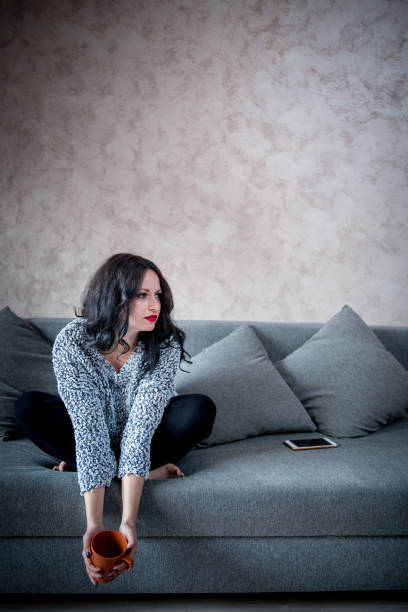 istock Woman sitting on couch with mug in hands 1026069508