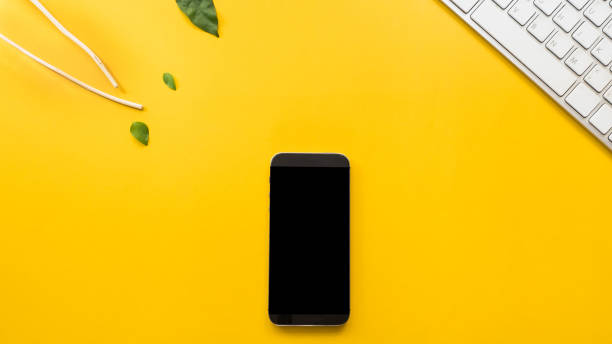 istock Smartphone  with keyboard and leaves on yellow background business  concept desk table copyspace 1026089864