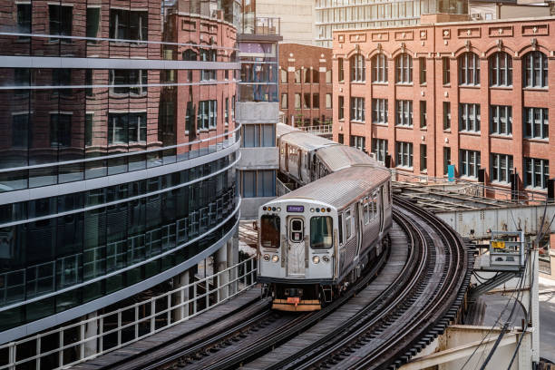Chicago CTA Train between City Buildings Chicago typical silver colored commuter train moving on elevated tracks to railroad station in between urban city buildings of Chicago, Illinois, USA. elevated train tracks stock pictures, royalty-free photos & images