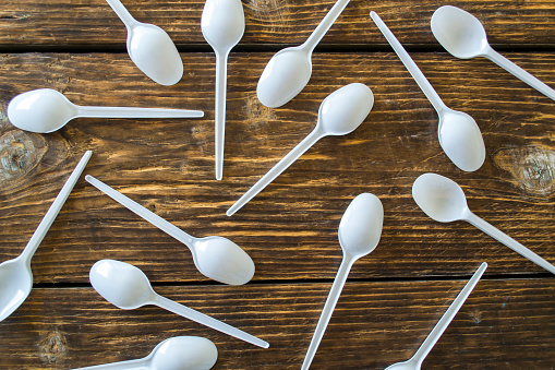 White plastic spoons on a wooden background.
