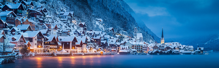 Panorama view of famous Hallstatt lakeside town in the Alps in mystic twilight during blue hour at dawn on a beautiful cold foggy day in winter, Salzkammergut region, Austria