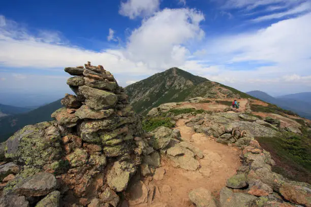 Hikers trekking along Franconia mountain ridge traverse, with a beautiful landscape background and blue sky. Mount Lafayette, Mount Lincoln, New Hampshire, USA