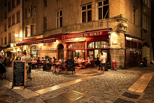 Lyon, France  - August 21, 2018: Colorful saint Jean district in old Lyon, the famous and typical old town of the city of Lyon by night. People on the terrace of typical restaurant. Duboeuf famous restaurant of Lyon.