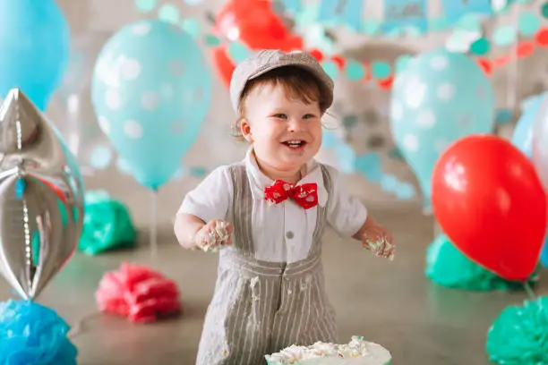 Baby boy touching his first birthday cake. Making messy cakesmash in decorated studio location.