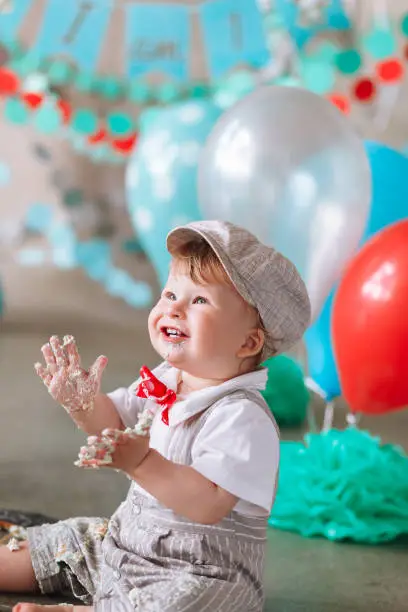 Little boy looking side with mouth covered in white icing and cake in decorated studio backdrop. Birthday cakesmash party.