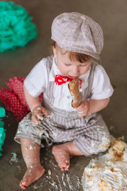 Little boy eating cake in messy decorated studio backdrop. Birthday cakesmash party.