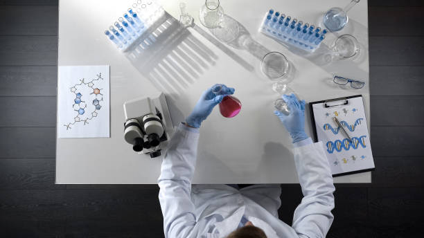 istock Laboratory worker examining purple liquid in flask, adding reagent, top view 1026202736