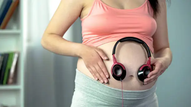 Photo of Woman putting earphones on her pregnant belly, enjoying favorite music with baby