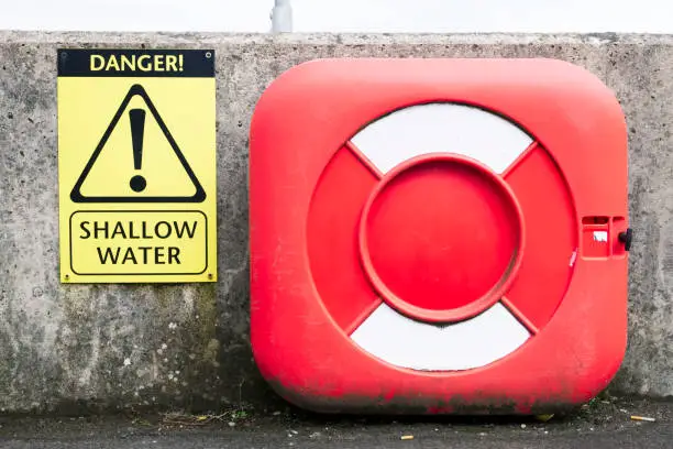 Shallow water sign and red life safety buoy at harbour wall uk