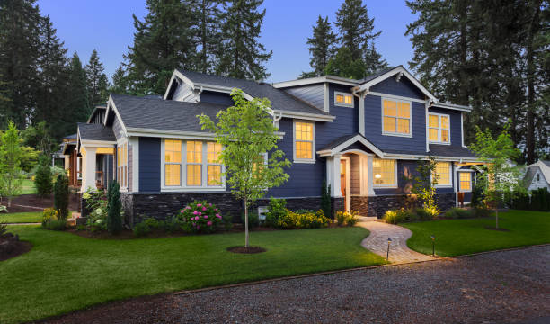 Beautiful luxury home exterior at twilight facade of home with manicured lawn, landscaping, and backdrop of trees and dark blue sky. Glowing interior lights create a welcoming mood. gable photos stock pictures, royalty-free photos & images