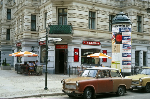 Berlin (East), Germany, 1986. Old Berlin corner pub on the Sredzkistraße / Husemannstr. in the district Prnzlauer Berg. Furthermore: cars, house and guests on the terrace of the pub.