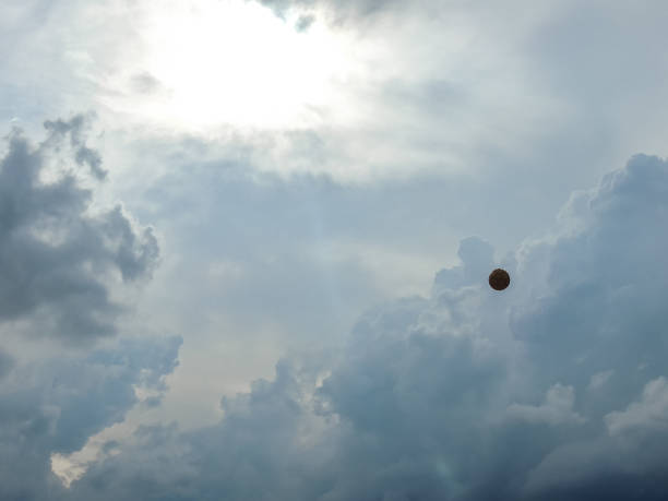 Photograph of a soccer ball in the sky with a beautiful cloudscape, with giant clouds during the afternoon, and the sunlight behind the clouds.
