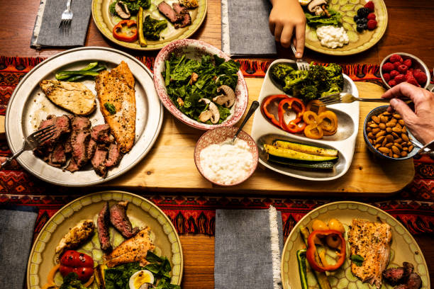 A ketogenic meal laid out on a dining table with the hands of people serving themselves A ketogenic meal laid out on a dining table with the hands of people serving themselves.  A keto diet is a low carb, high fat diet that avoids many fruits. ketogenic diet photos stock pictures, royalty-free photos & images