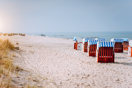 Blue striped roofed chairs on sandy beach in Travemunde in sun light. Dune grass in foreground. North Germany