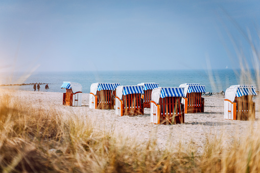 Blue striped roofed chairs on sandy beach on sunny day framed by dune grass in Travemunde. Germany
