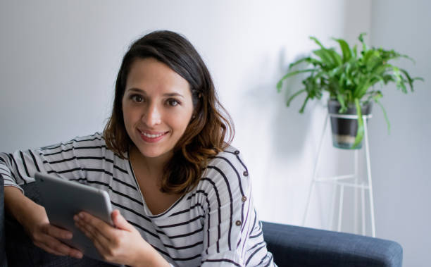 istock Young woman at home holding a tablet sitting on couch 1026258144