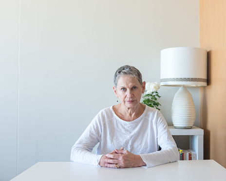 Beautiful older woman with short grey hair sitting at a table at home looking at camera (selective focus)