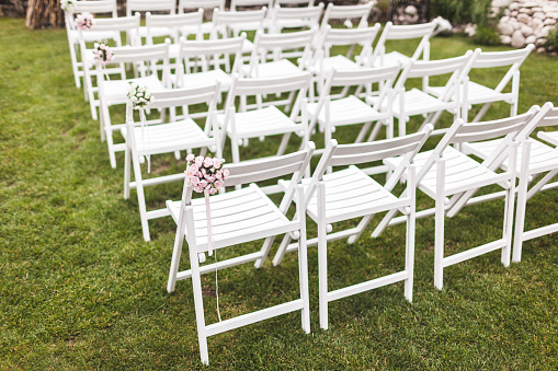 Cozy rustic wedding ceremony with wooden white chairs on green grass