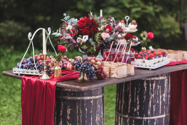 istock Wedding reception wooden table standing on two barrels, decorated with red flowers, sweets, drinks and silk. Rustic style 1026273416