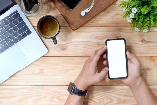 istock Man's hand using mobile smartphone on wooden desk and office supplies, Blank screen mobile phone for graphic display montage. 1026290610