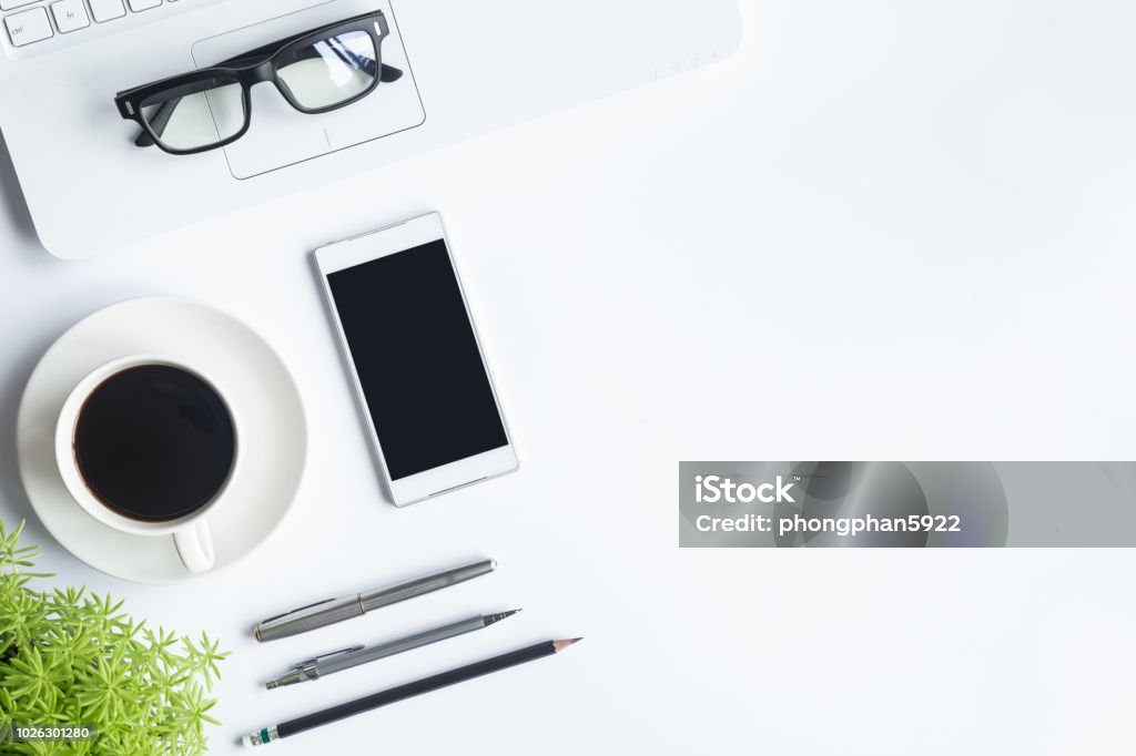 White desk office with laptop, smartphone and other supplies with cup of coffee. Top view with copy space for input the text. Designer workspace on desk top, view with essential elements on flat lay. Desk Stock Photo