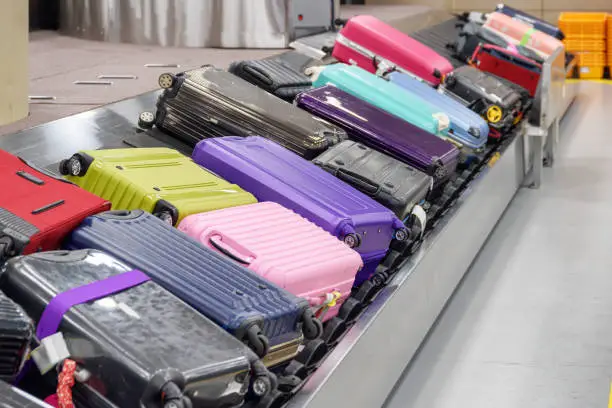 Bright suitcases on luggage conveyor belt at arrival area of passenger terminal in airport. View of baggage carousel.