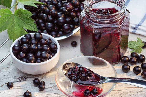 Jam or marmalade of black currant and currant with green leaves on light background.