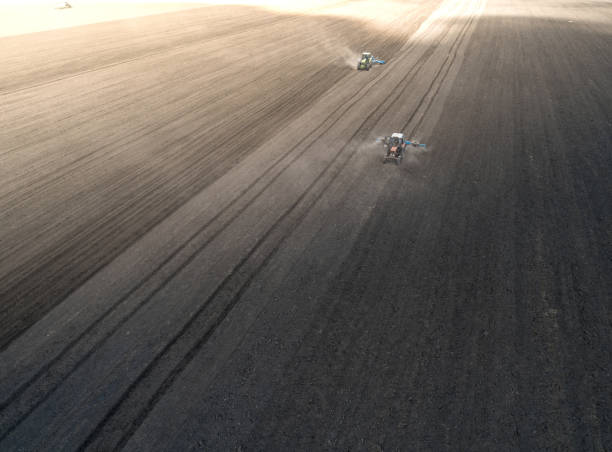 istock Two bright blue tractor plowing the ground against a black earth background. 1026409618