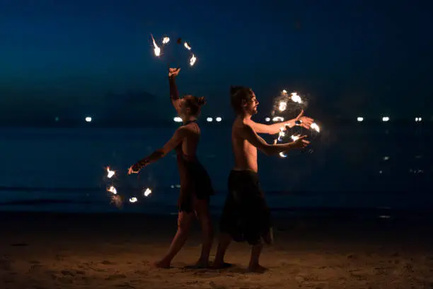 Beautiful, young man and woman performing fire dance on the beach.