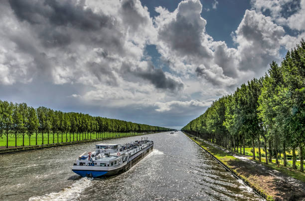 Inland barge on the Amsterdam-Rhine canal Inland barge on the long straight tree-lined Amsterdam-Rhine canal just south of Amsterdam on a day in summer with dramatic cloud formations barge stock pictures, royalty-free photos & images