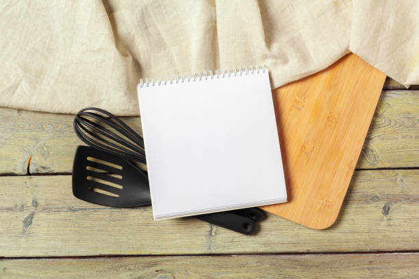 istock Blank sheet of opened notepad and kitchen utensils on  table with tablecloth, copy space 1026447584