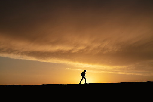 SIlhouette of a lonely woman walking at sunset on a hill.