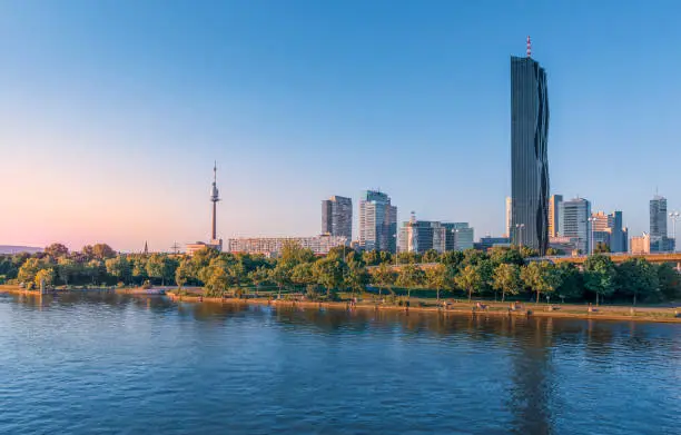 Beautiful cityscape with modern buildings, the tallest skyscraper in Austria and the blue Danube river, in the Donau district of Vienna, at sunset.