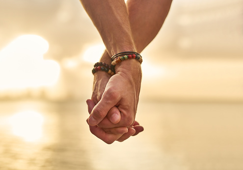Closeup shot of an unrecognizable couple holding hands while spending the day by the beach