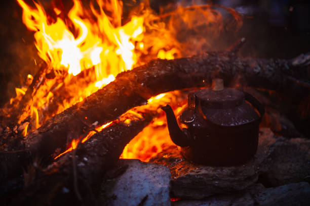 istock Boiling of tea in kettle on bonfire with large firewood. Tea drinking in open air. Active outdoor recreation. Camping in dusk. Romantic warm atmosphere in twilight on nature. Active rest. 1026485520