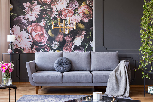Colgante oro industrial ligero y negro muebles en un interior oscuro salón con papel pintado de flores y un sofá gris photo