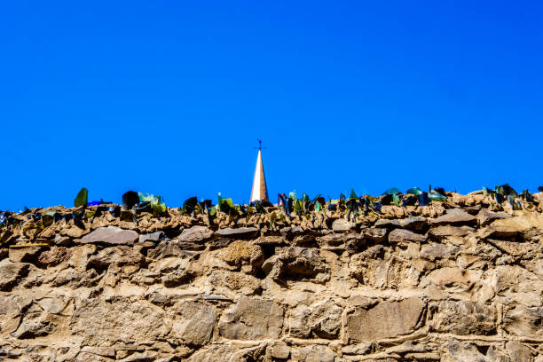 Stone wall with anti climb glass Broken glass on top of stone wall as anti climb measure with church steeple against clear blue sky sentinel spire stock pictures, royalty-free photos & images