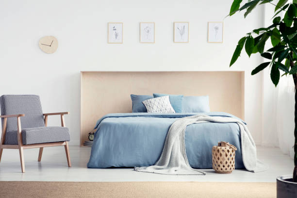 istock Patterned armchair next to blue bed with blanket in natural bedroom interior with posters. Real photo 1026515436