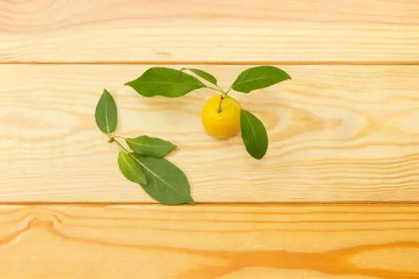 One yellow cherry plum with leaves on a light colored wooden surface