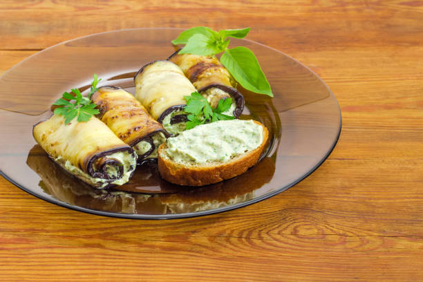 Fragment of the dark glass dish with eggplant rolls with filling of tuna and processed cheese and open sandwich with stuffing on the old rustic table