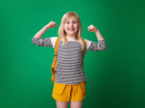 istock smiling pupil with backpack on green background showing biceps 1026541078