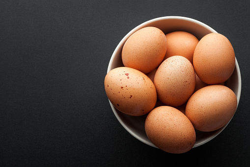 brown eggs in bowl isolated on dark background. top view