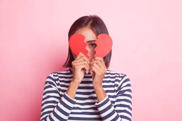 Beautiful young Asian woman with broken heart on pink background